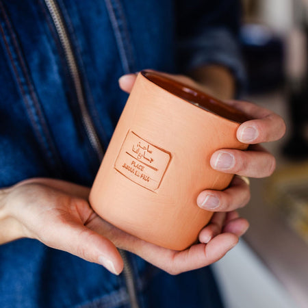 Person holding a terracotta pot with text on it, wearing a blue denim jacket.
