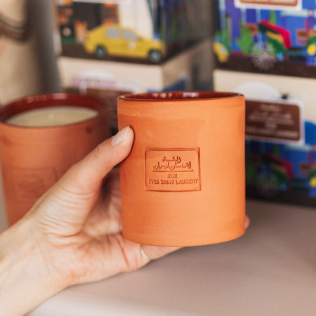 Person holding a terracotta candle with more candles and boxes in the background