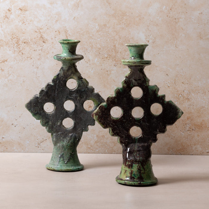 Two green ceramic candle holders with intricate designs on a beige surface and background.