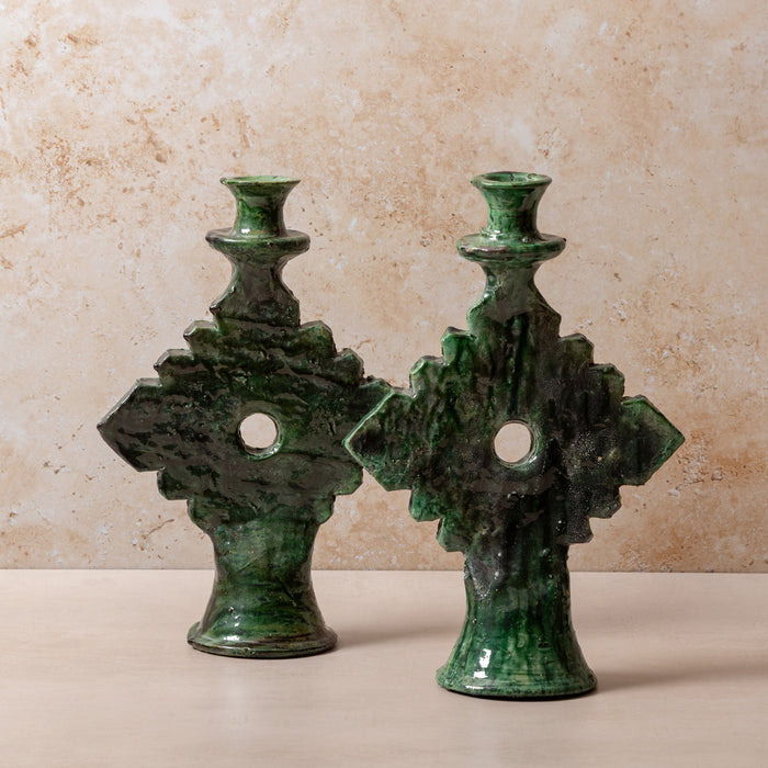 Pair of green ceramic candle holders on a beige surface with a beige background
