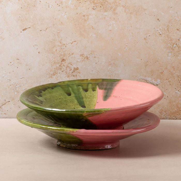 Two ceramic bowls with pink and green glaze on a beige surface.