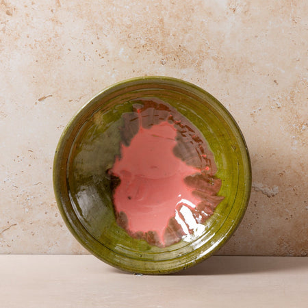 Green ceramic bowl with pink interior on a beige stone surface