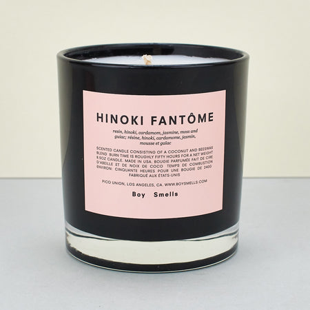 black candle with a pink label and text across a plain background. 