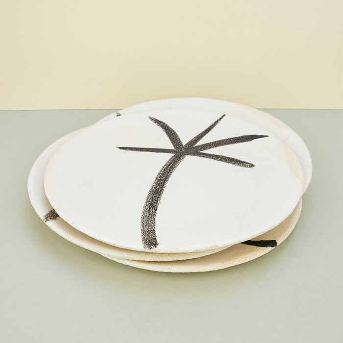 stack of white plates with black palm tree drawing on plain background