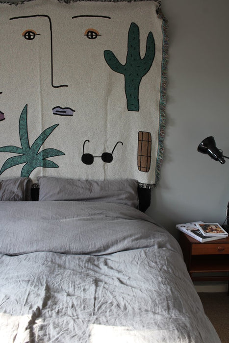 wall hanging blanket with a face and sunglasses hanging above a bed 