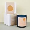 moroccan black candle with an orange label with an outline of morocco. next to a white candle box with an orange cover. 