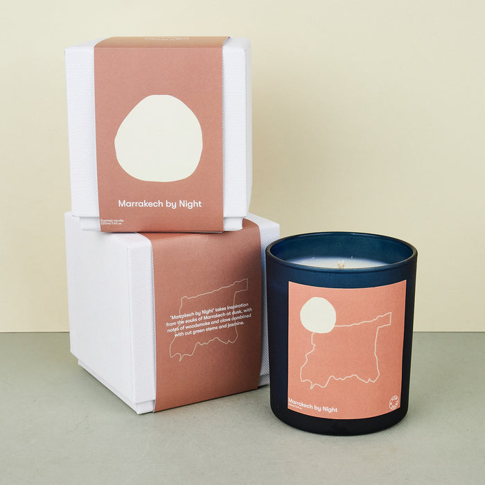 moroccan black candle with a pink label with an outline of morocco. next to a white candle box with a pink cover. 