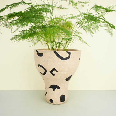rustic ceramic plant pot in beige with black geometric decorations with a plant in it. 