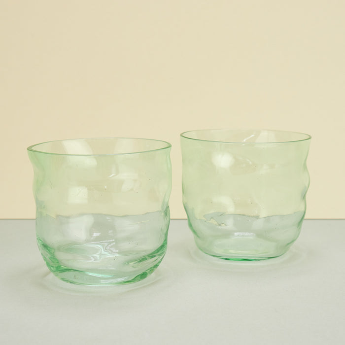 two glasses next to each other with a hint of green on a plain background. 