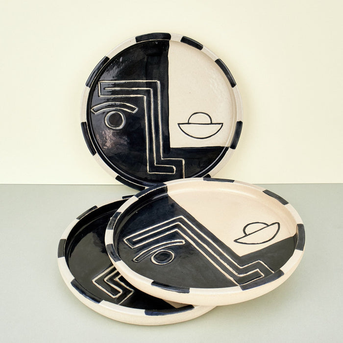 black and white plates with faces on them in a geometric manner. plates stacked on a plain background. 