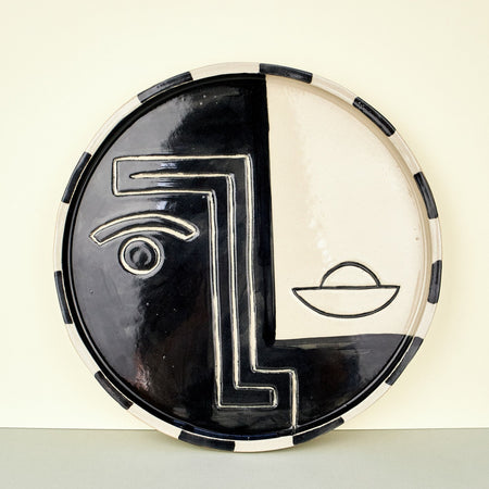 black and white plates with faces on them in a geometric manner. plate leaning on a plain background. 
